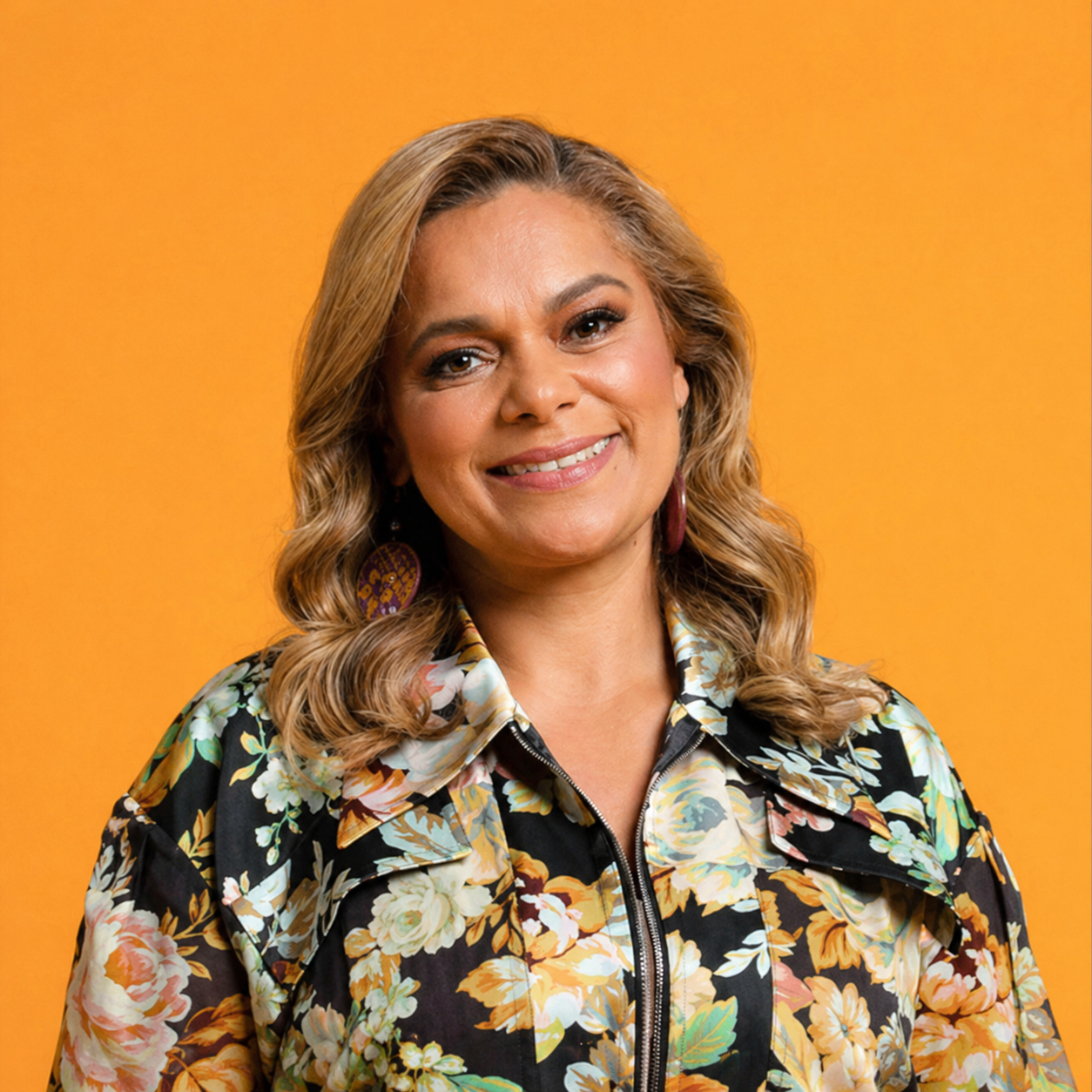 Woman with wavy hair smiling against orange background wearing floral jacket